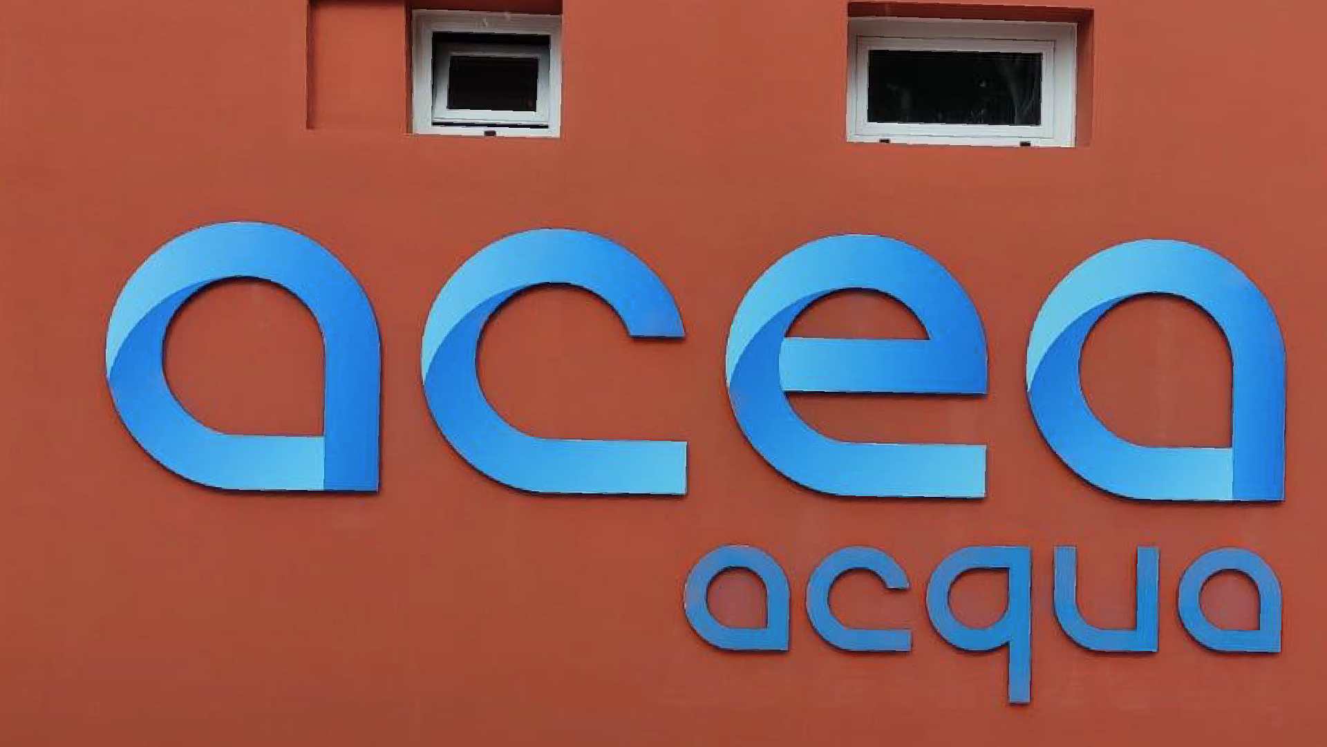 Logo di Acea acqua in azzuro applicato su una parete color rosso spento